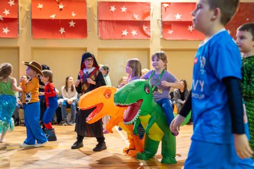 Dzieci w kolorowych strojach podczas zabawy. Dwa dmuchane dinozaury.