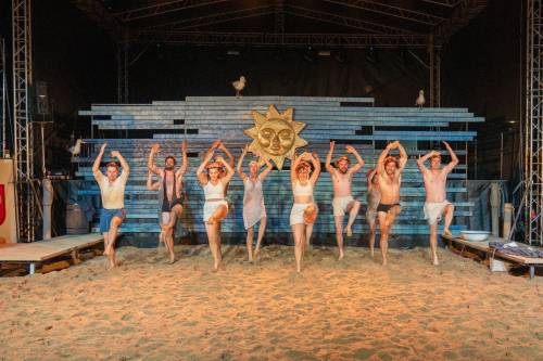 Aktorzy w piasku na scenie tańczą kankana.