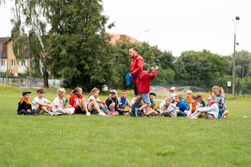 Dzieci podczas zabaw na boisku. Grupa siedzi na trawie.