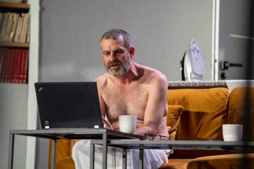 Aktor bez koszulki siedzi przed komputerem.
