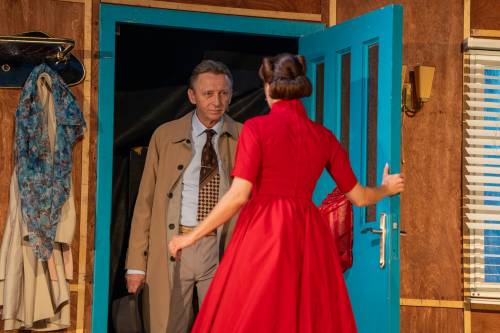 Kobieta w czerwonej sukience otwiera drzwi mężczyźnie.