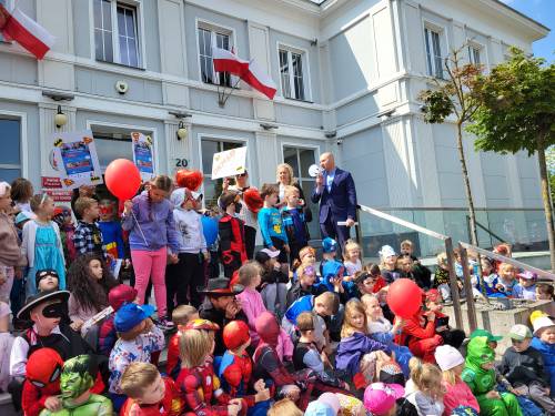 Dzieci w strojach superbohaterów siedzą na schodach Urzędu Miasta.