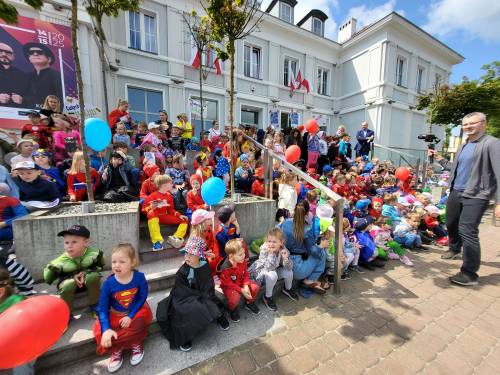 Dzieci w strojach superbohaterów siedzą na schodach Urzędu Miasta.