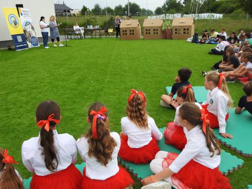 Dzieci w biało-czerwonych strojach siedzą na trawie