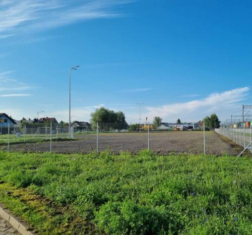 Ogrodzona działka, na której powstanie nowy parking, na pierwszym planie widać zieleń