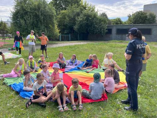 Dzieci siedzą na kolorowej macie i słuchają policjantki