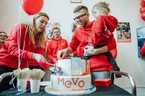 Uroczystość, czerwone stroje, mężczyzna z dzieckiem na ręku i kobietą kroją tort.