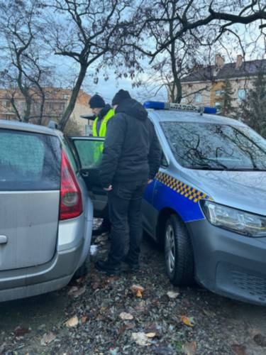 Dwie postacie stojące przy aucie z otwartymi drzwiami