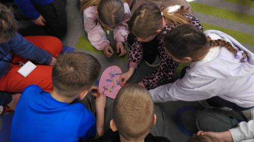 Dzieci siedzą na podłodze i przyklejają słowa na papierowe serce