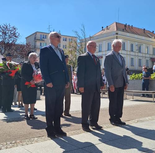 Uczestnicy obchodów stoją pod pomnikiem Nike