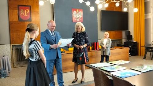 Zastępca burmistrza ogląda jedną z nagrodzonych prac, obok stoją - kierownik biblioteki i laureatka