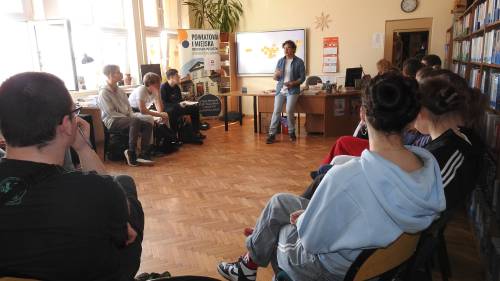 Uczestnicy projektu siedzą w sali na krzesłach słuchając, co mówi prowadzący spotkanie