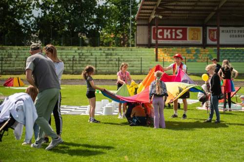 Grupa dzieci na trawie trzyma w rękach dużą, kolorowa chustę