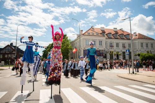 Trójka szczudlarzy prowadzi pochód ludzi ulicą