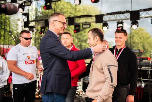 Burmistrz miasta zakłada medal mężczyźnie na szyję, w tle inni zawodnicy