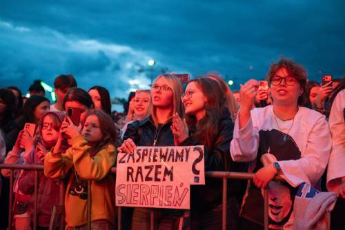 Grupa osób za barierkami z kartką z napisem