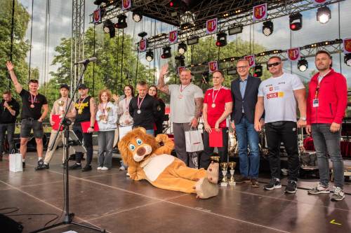 Grupa nagrodzonych zawodników na scenie z burmistrzem i maskotką lwem