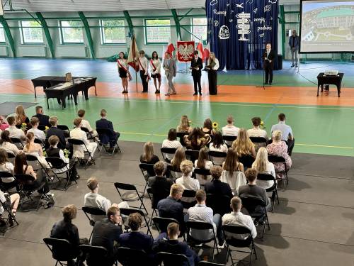 Widok na salę pełną siedzących uczniów i prowadzących wydarzenie