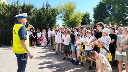 Policjant z mikrofonem w ręku stroi przed grupą uczniów