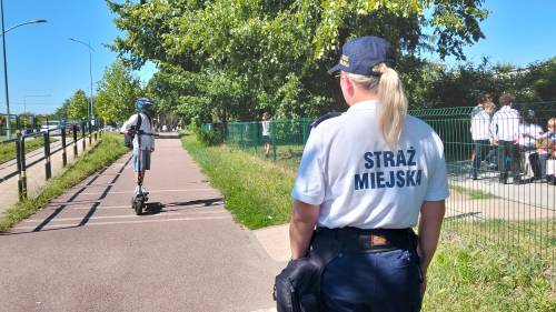Strażniczka miejska patrzy na chłopca jadącego hulajnogą po ścieżce rowerowej