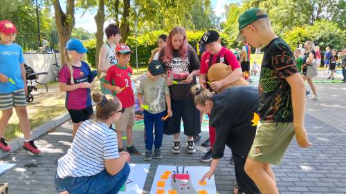 Dzieci i panie pochylają się na rysunkami, które są na ziemi