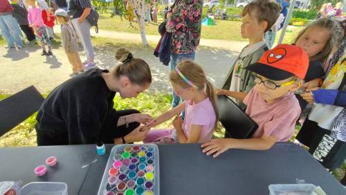 Animatorka tworzy na ręku dziewczynki tatuaż, inne dzieci stoją w kolejce