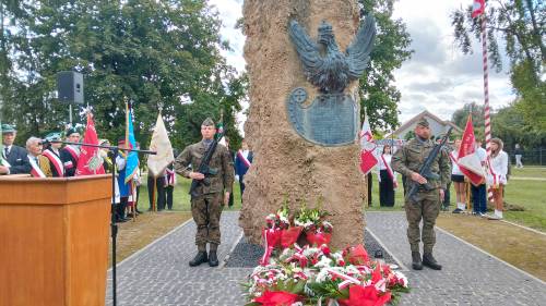 Widok na pomnik z kwiatami i dwóch żołnierzy