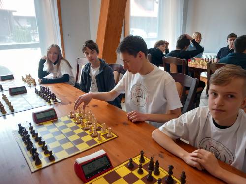 Młodzież siedząca przy stole z rozłozonymi szachownicą i szachami, czekają na rozpoczęcie gry.